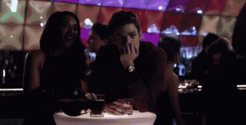 a man and a woman are sitting at a table in a bar with drinks .
