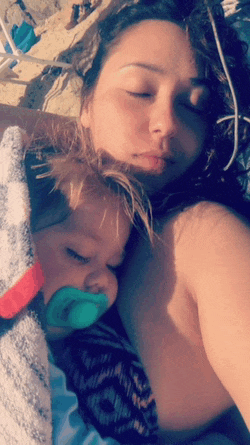 a woman laying on the beach with a baby with a pacifier in her mouth
