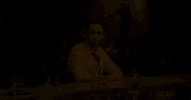 a man in a white shirt and tie sits at a bar with a drink in front of him