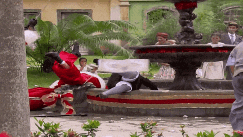a man in a red costume is laying on the ground in front of a fountain