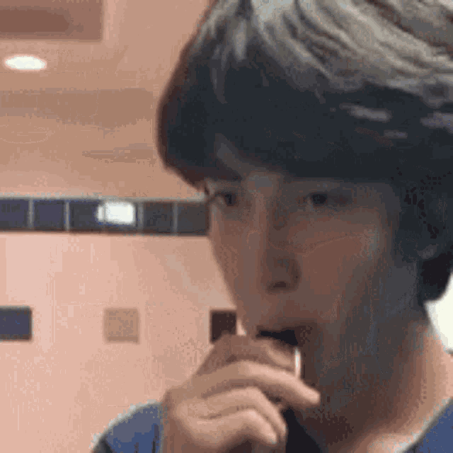 a young man is brushing his teeth in a bathroom while holding a toothbrush in his mouth .