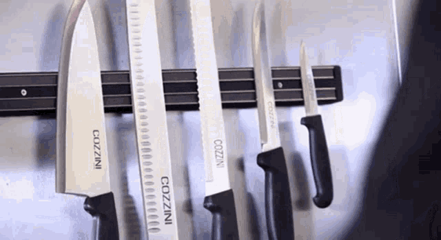 a row of cozzini knives are lined up on a magnetic knife rack