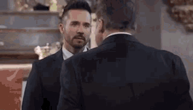 two men in suits are standing next to each other in a room and talking to each other .