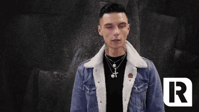 a man wearing a denim jacket with a fur collar is standing in front of a black background .