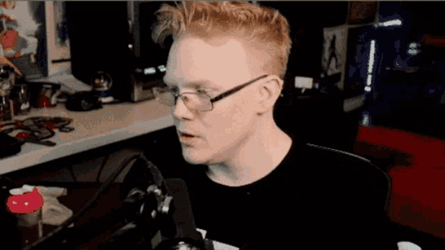 a man with glasses is sitting in front of a microphone with his mouth open