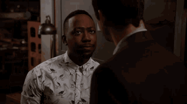 a man wearing a white shirt with birds on it is talking to another man in a suit