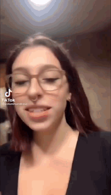 a woman wearing glasses and a nose ring is talking on a tiktok video .