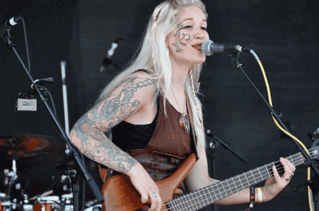 a woman with a tattoo on her face singing into a microphone while holding a guitar