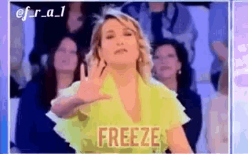 a woman in a yellow shirt is making a freeze gesture while standing in front of a crowd .