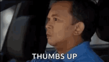 a man is sitting in a car and giving a thumbs up .