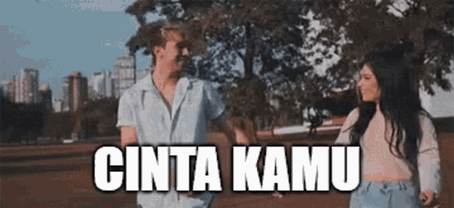 a man and a woman are holding hands in a park with the words cinta kamu written above them .