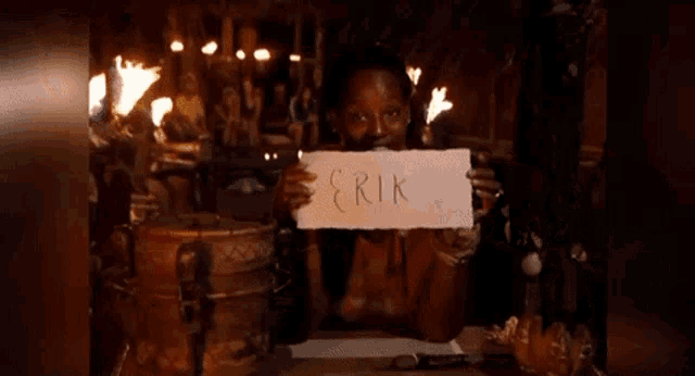 a woman is holding a piece of paper with the name erik written on it in front of her face .