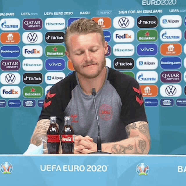 a man sitting at a table with two coca cola bottles in front of a uefa euro 2020 sign