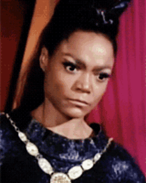 a woman wearing a necklace and a crown looks at the camera