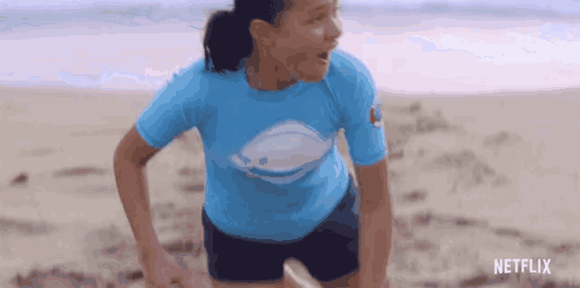 a girl wearing a blue shirt with a whale on it is running on the beach with a netflix logo in the corner