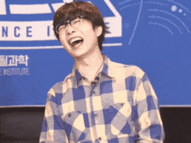 a man wearing glasses and a plaid shirt laughs in front of a sign that says science institute