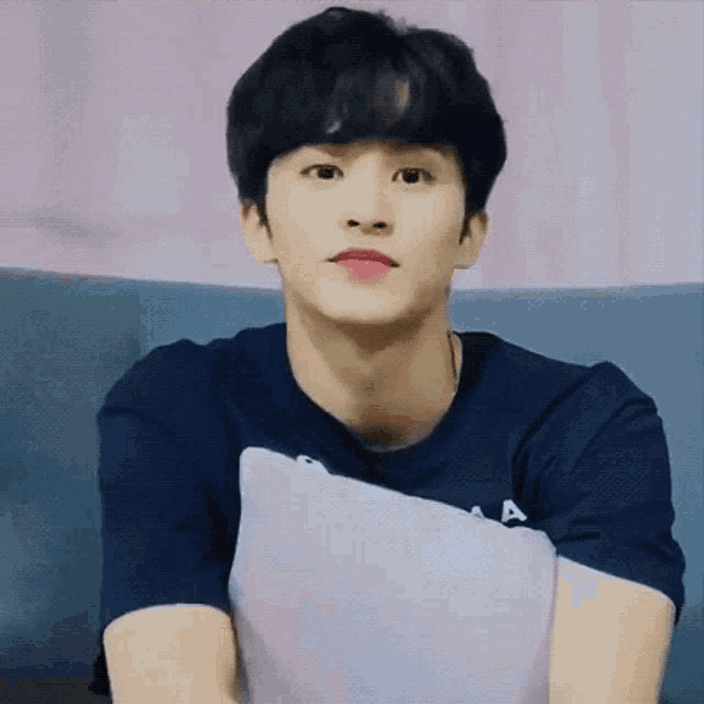 a young man in a blue shirt is sitting on a couch holding a pillow .