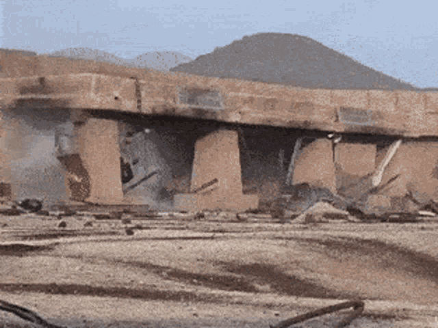 a building is being demolished in the desert with mountains in the background