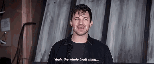 a man in a black jacket is smiling and talking to someone .