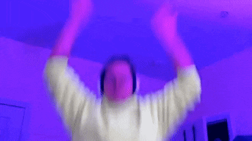 a man wearing headphones is raising his arms in the air in a room with purple lights .