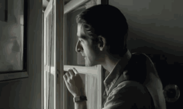 a man looking out a window with a watch on his wrist