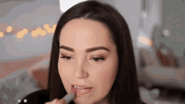 a woman is applying lipstick to her lips in a living room .