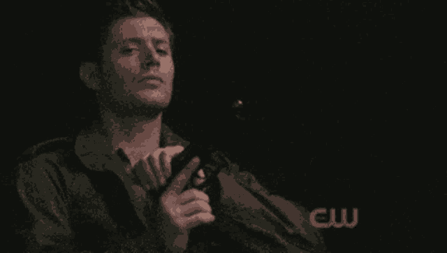 a man holding a gun in front of a cw sign