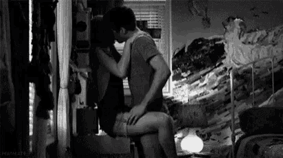 a man and a woman are kissing in a room in front of a window .