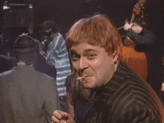 a man with red hair is giving a thumbs up sign while sitting in a dark room .