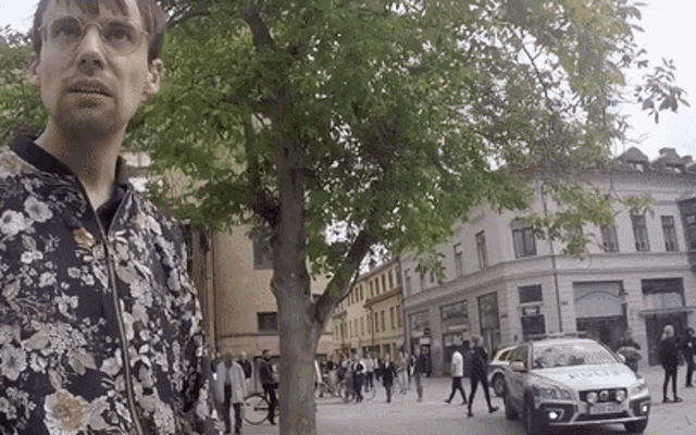 a man in a floral jacket is standing in front of a police car that says polis