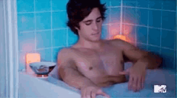 a shirtless man is taking a bath in a bathtub with a mtv logo behind him