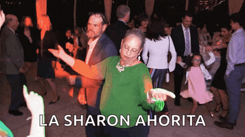 a woman in a green shirt is dancing in a crowd with the words la sharon ahorita written above her