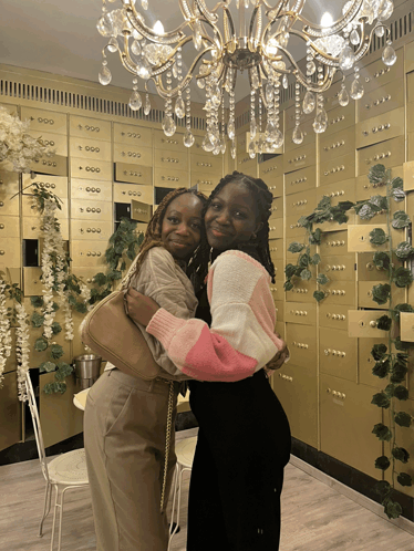 two women are hugging in front of a wall of gold lockers with numbers on them