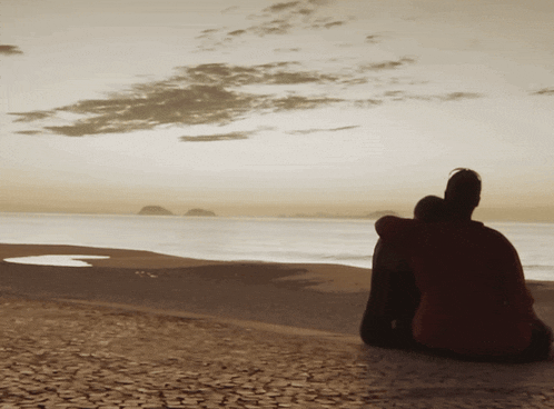 a couple sitting on a beach looking out over the ocean