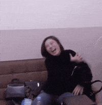 a woman in a black sweater is sitting on a couch and laughing .