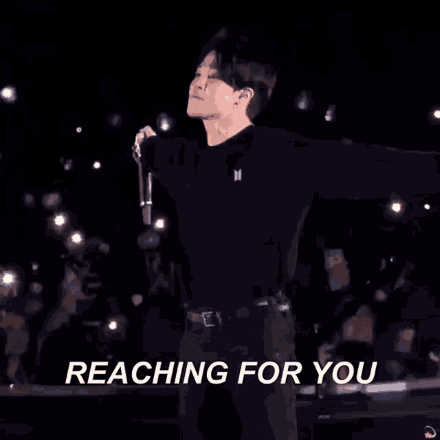 a man singing into a microphone with the words " reaching for you " above him