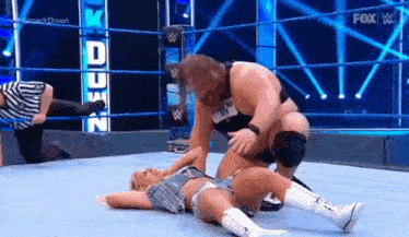 a woman is laying on the ground in a wrestling ring while a man is kneeling over her .