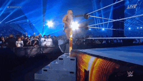a wrestler is jumping over a rope in a wrestling ring while a crowd watches .
