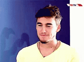 a man in a yellow shirt is making a funny face in front of a tv screen .