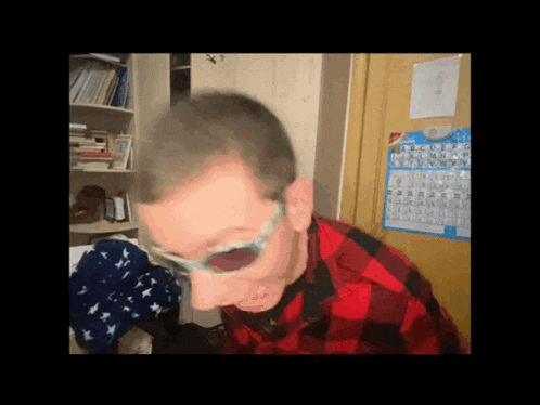 a man wearing glasses and a plaid shirt is standing in front of a periodic table calendar