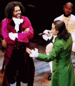 a man in a green coat is singing into a microphone while another man in a red coat stands behind him