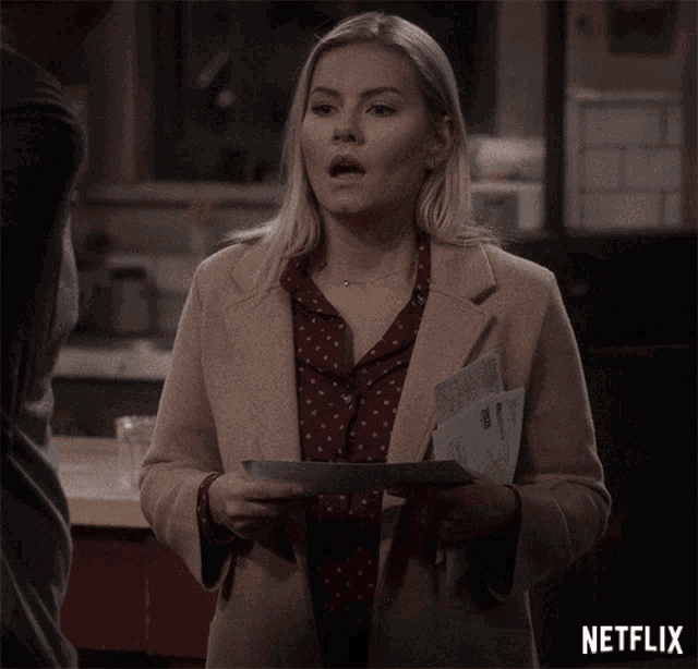 a woman in a tan coat is holding a piece of paper with a netflix logo in the corner