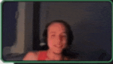 a man wearing headphones and a red tank top is laughing while sitting in front of a computer screen .