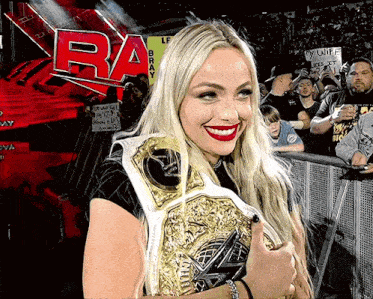 a woman is holding a wrestling championship belt in front of a sign that says ' raw ' on it