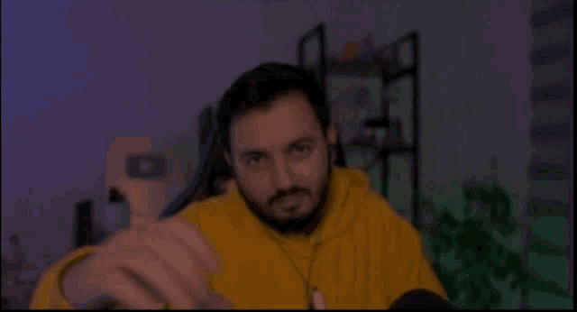 a man with a beard wearing a yellow hoodie is sitting in a chair .