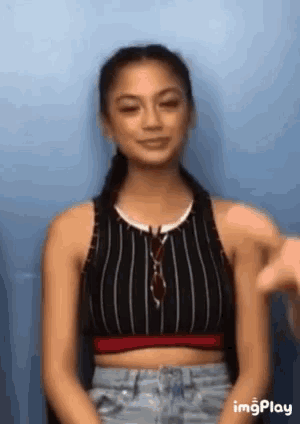 a woman in a striped crop top is sitting in front of a blue wall and smiling .