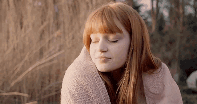 a woman with red hair is wrapped in a pink blanket with her eyes closed .