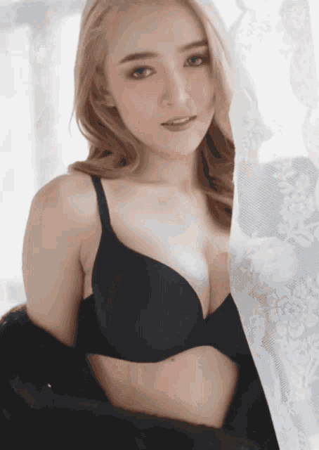a woman in a black bra stands next to a white curtain