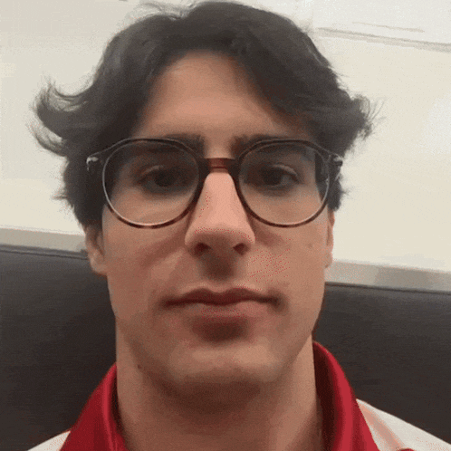 a young man wearing glasses and a red shirt is looking at the camera
