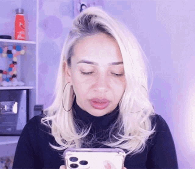 a woman with blonde hair and hoop earrings is looking at her phone